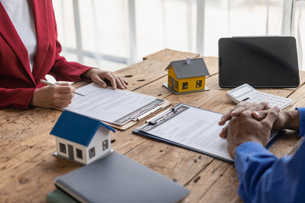 Real estate agents offer contracts to buy or rent housing. Businessman holding model small building house with property insurance at table in home sales office